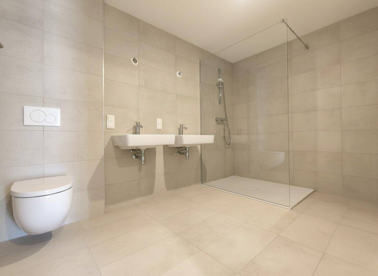 Modernes Badezimmer mit beigefarbenen Fliesen, Doppelwaschbecken und einer geräumigen begehbaren Dusche.