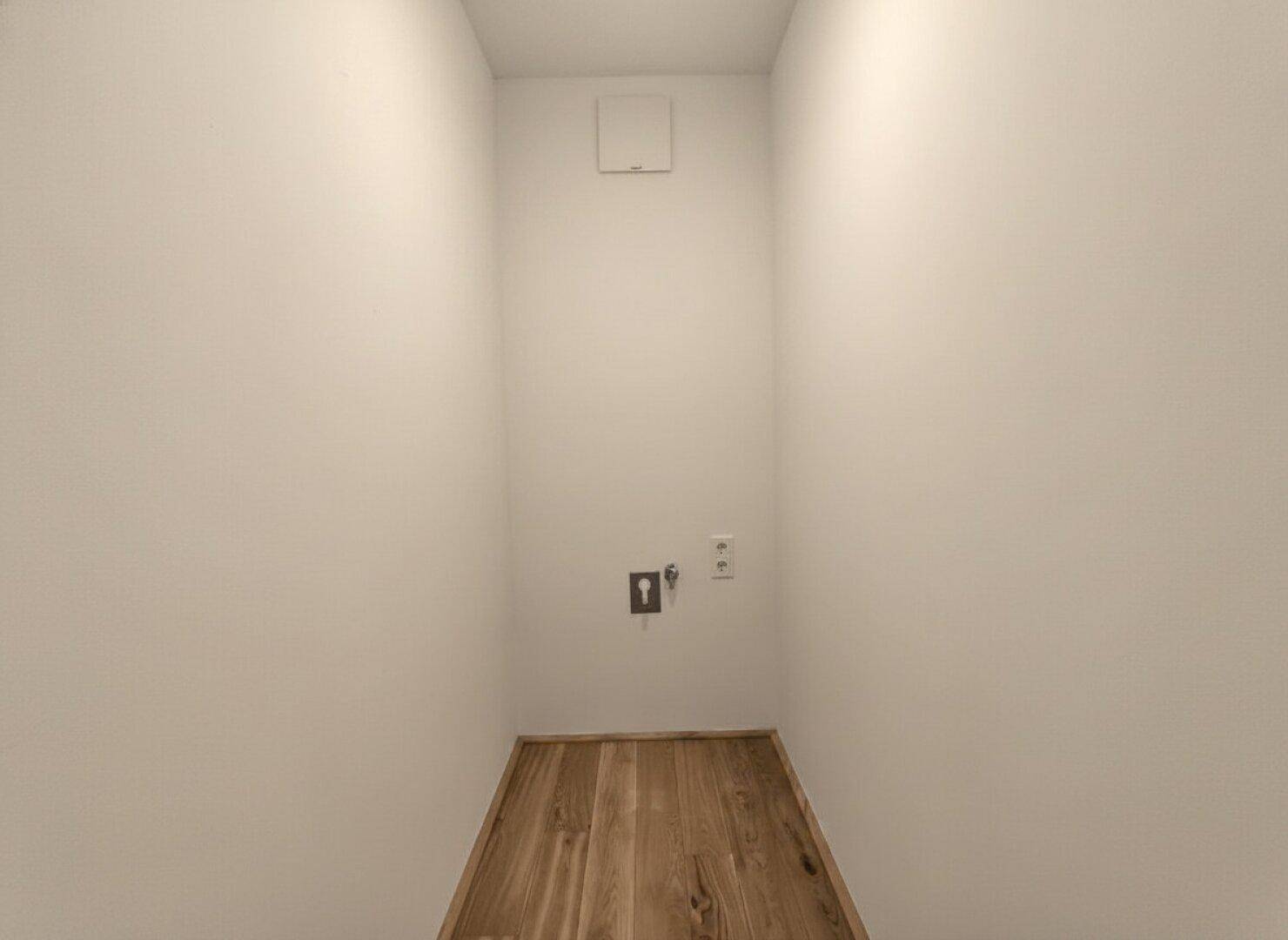 Praktischer Hauswirtschaftsraum mit Holzboden und Anschlüssen für Waschmaschine und Trockner.
