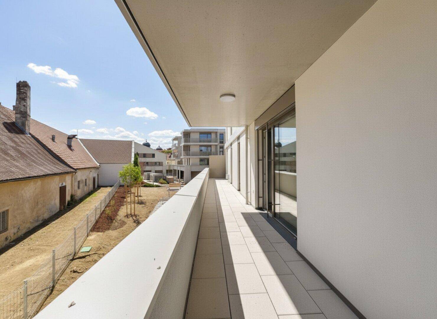 Moderner Balkon mit Fliesenboden und Blick auf die umliegende Neubausiedlung und Grünflächen.