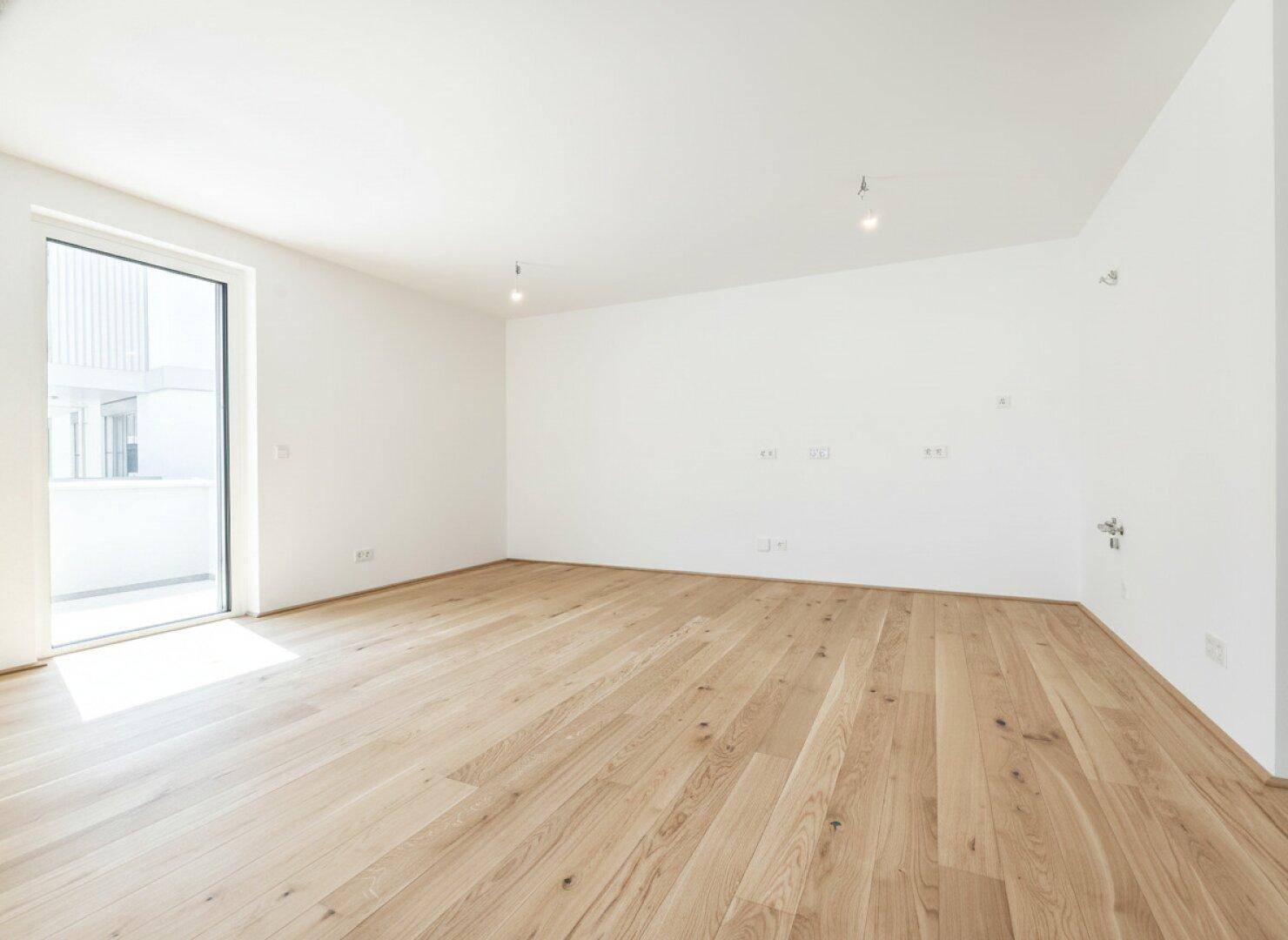 Geräumiges, helles Zimmer mit Holzboden und großem Fenster, bereit zur individuellen Gestaltung.