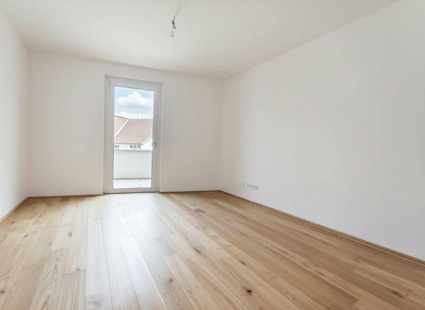 Helles Schlafzimmer mit Eichenparkett und Zugang zu einem kleinen Balkon.