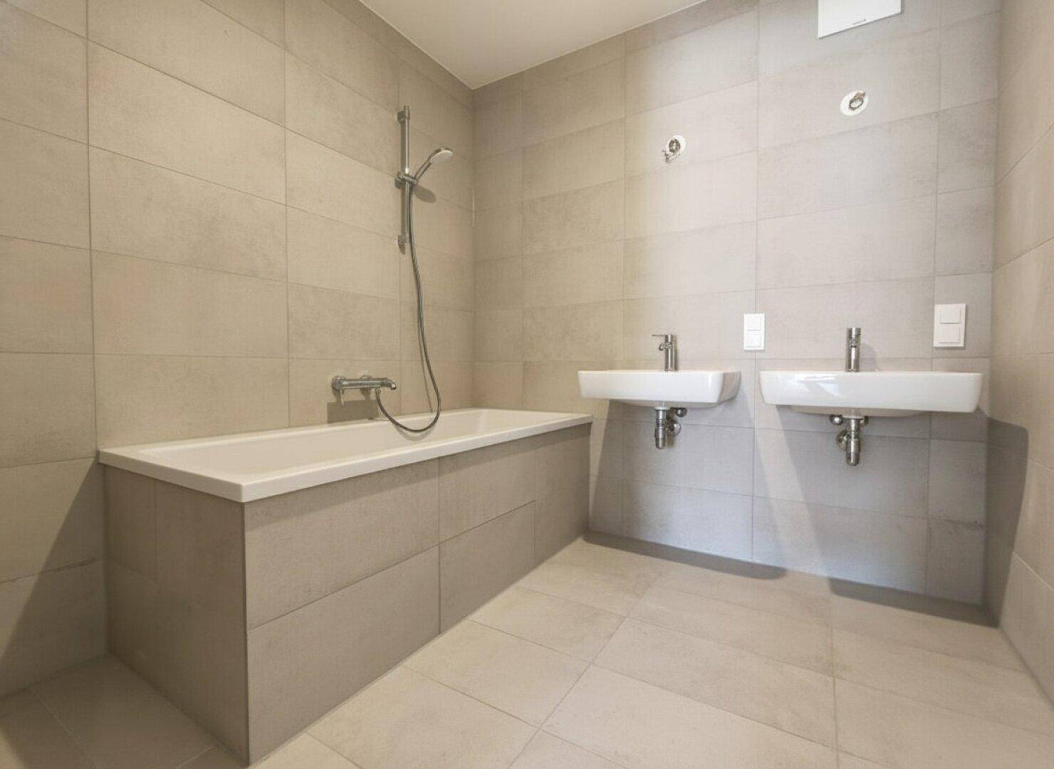 Modernes Badezimmer mit zwei Waschbecken, Badewanne und hellen Fliesen.