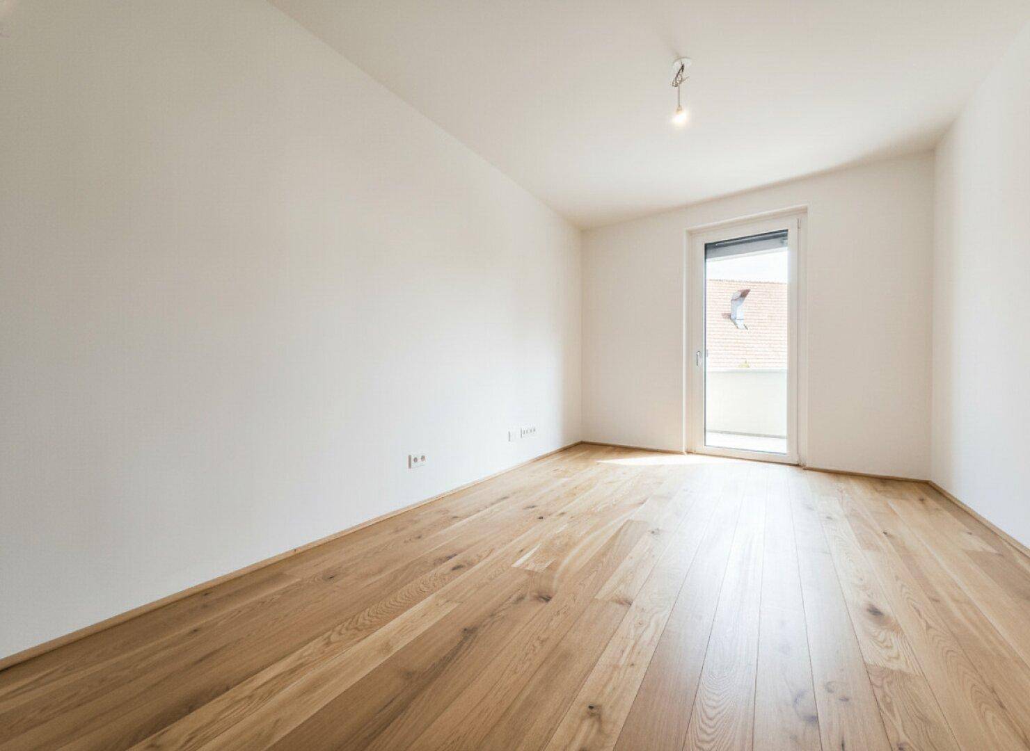 Geräumiges Schlafzimmer mit Holzboden und Balkonzugang, ideal für erholsame Nächte.
