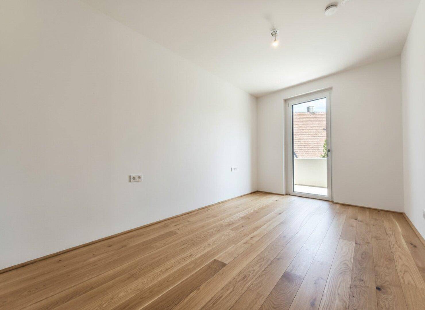 Lichtdurchflutetes Schlafzimmer mit Eichenparkett und Zugang zu einem Außenbereich.