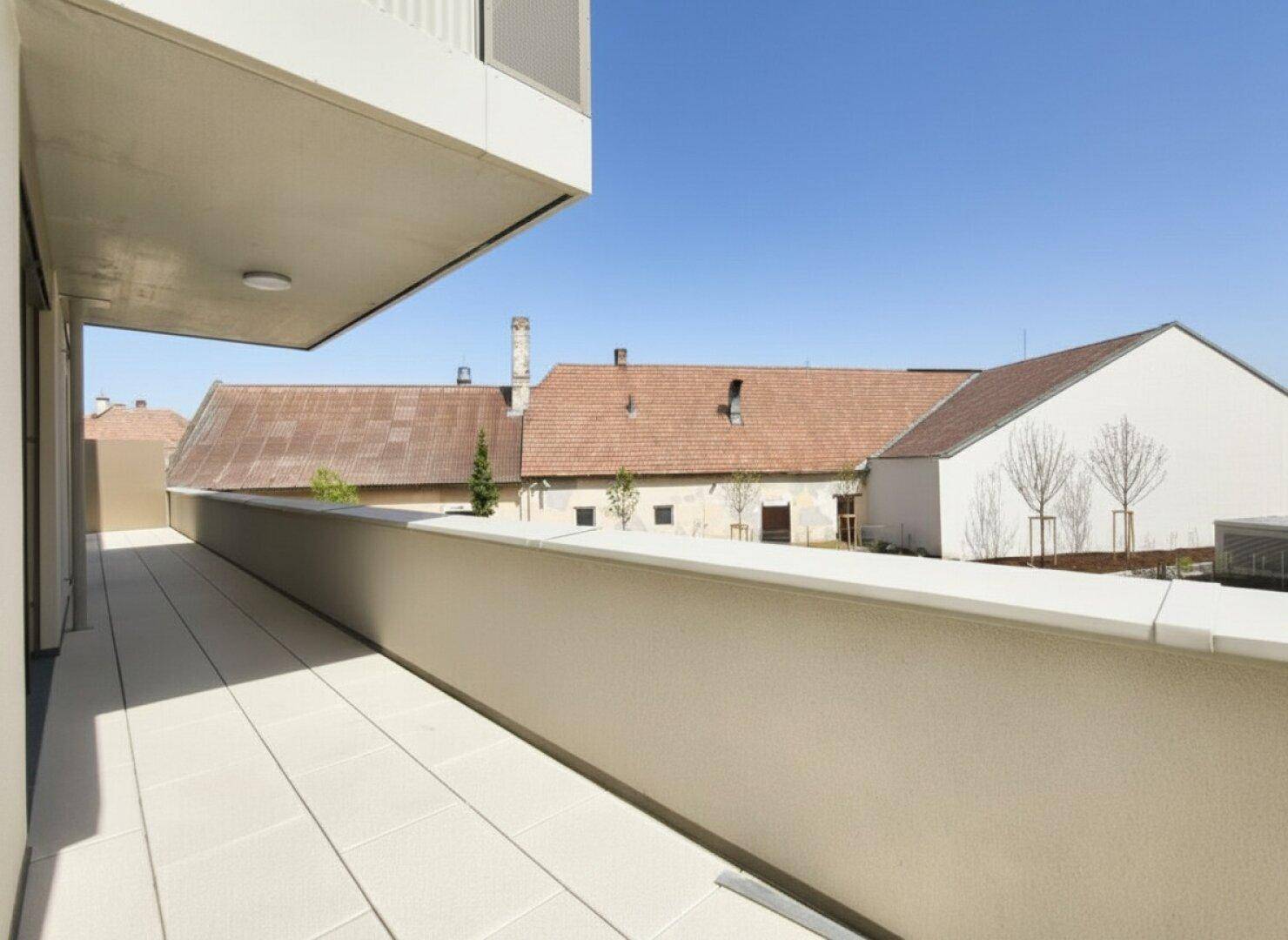 Langer Balkon mit Fliesenboden und Blick auf traditionelle Dächer unter blauem Himmel.