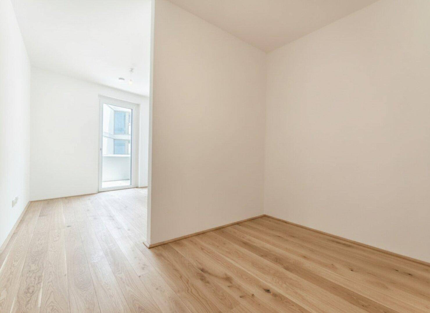 Helles Zimmer mit Holzboden und weiß gestrichenen Wänden, mit Zugang zu einem Balkon.