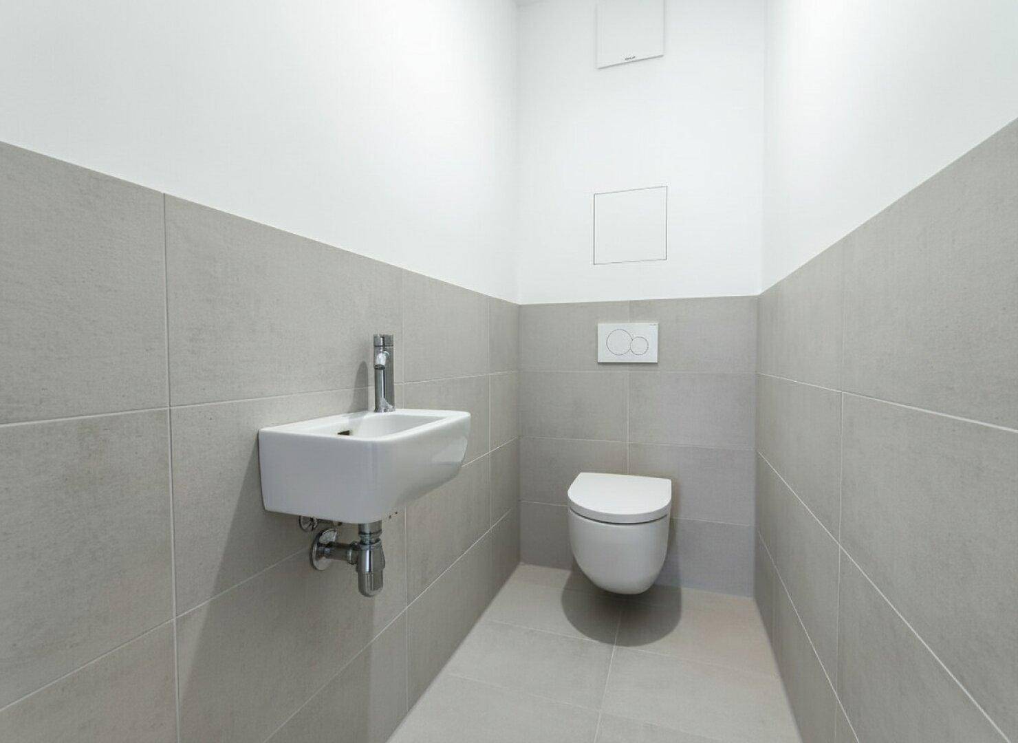Kleines Gäste-WC mit grauen Fliesen, wandhängender Toilette und kompaktem Waschbecken.