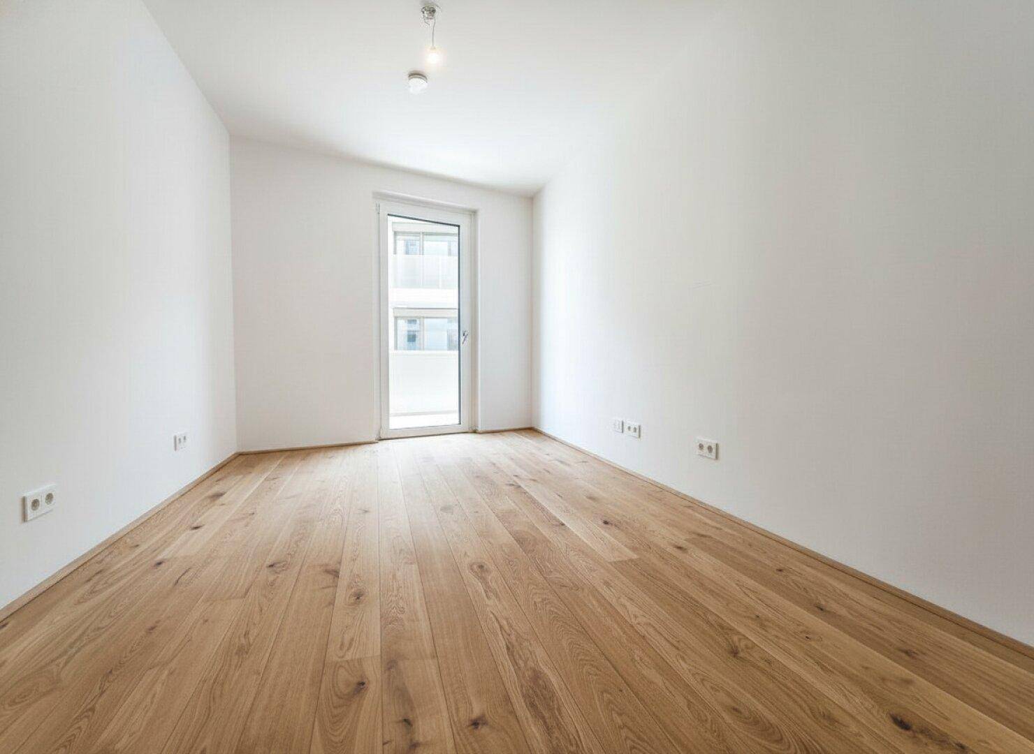 Modernes Schlafzimmer mit hellem Holzboden und Balkontür, bereit zur individuellen Gestaltung.