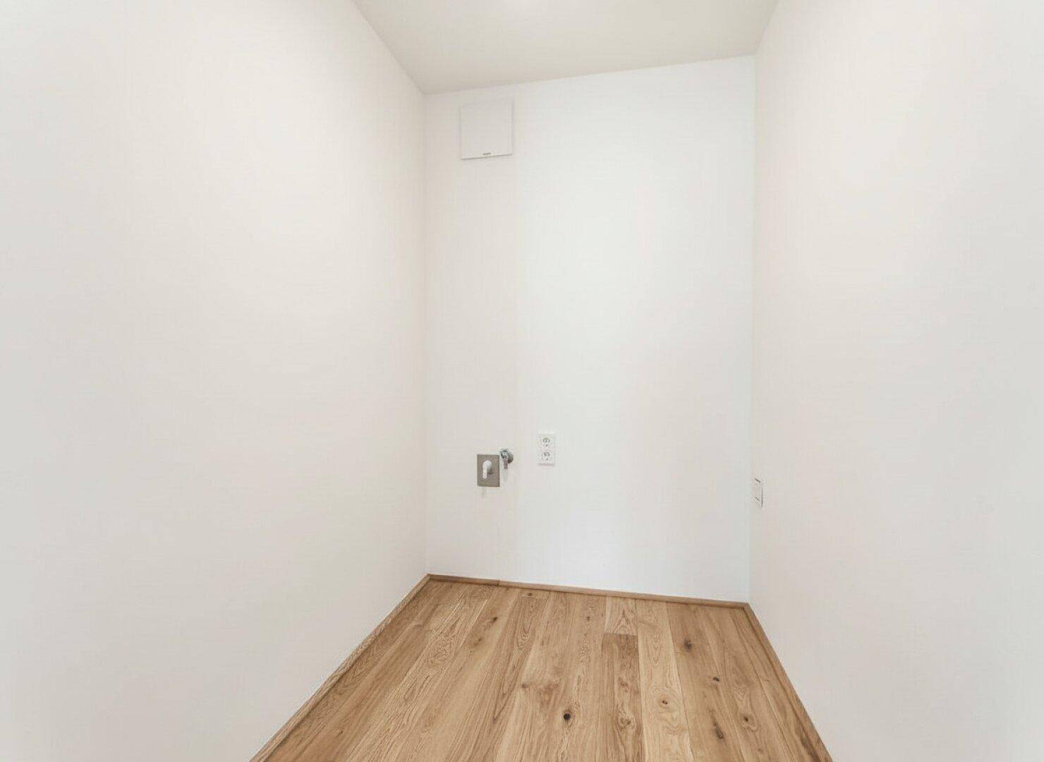 Praktischer Hauswirtschaftsraum mit Holzboden und Anschlüssen für Waschmaschine und Trockner.