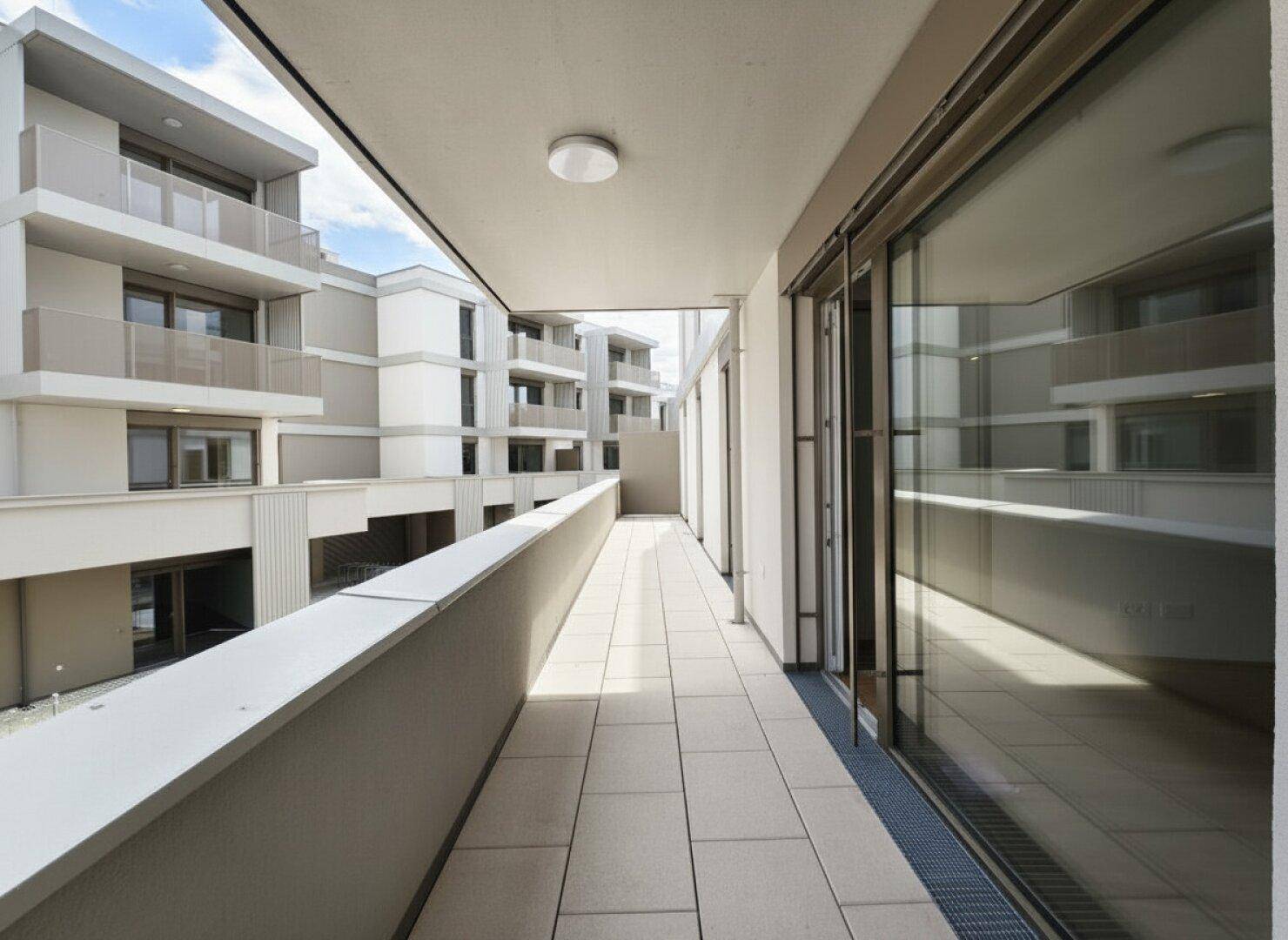 Heller Balkon mit Fliesenboden und Blick auf die umliegenden Neubauten unter blauem Himmel.