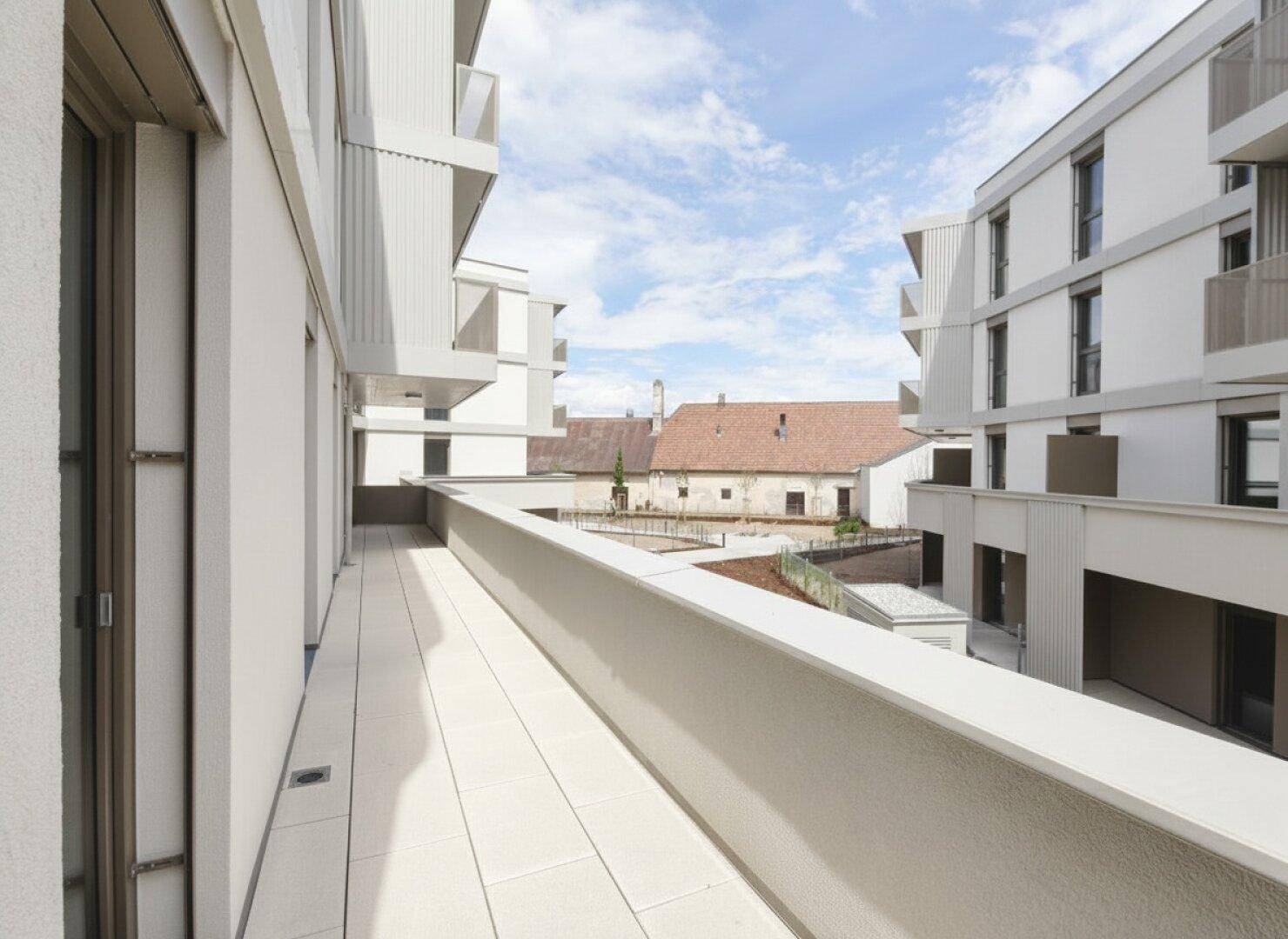 Langer, schmaler Balkon mit Fliesenboden und Blick auf moderne sowie historische Gebäude.