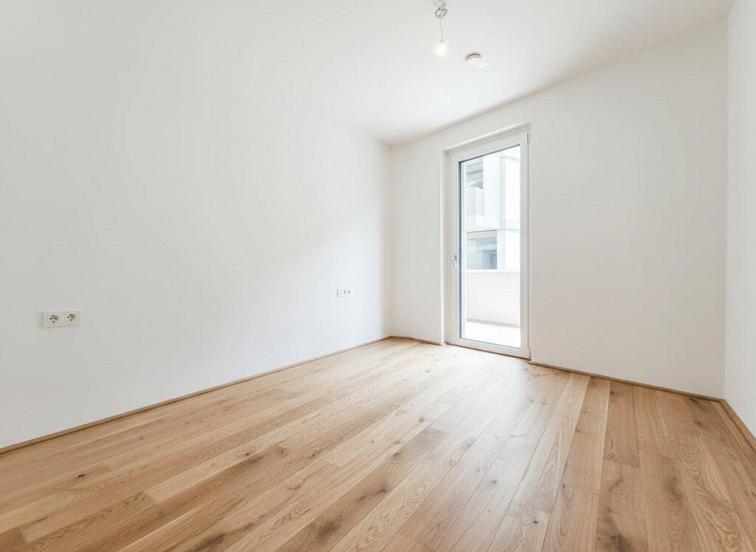 Helles Schlafzimmer mit Holzboden und Balkonzugang, ideal für Ruhe und Entspannung.