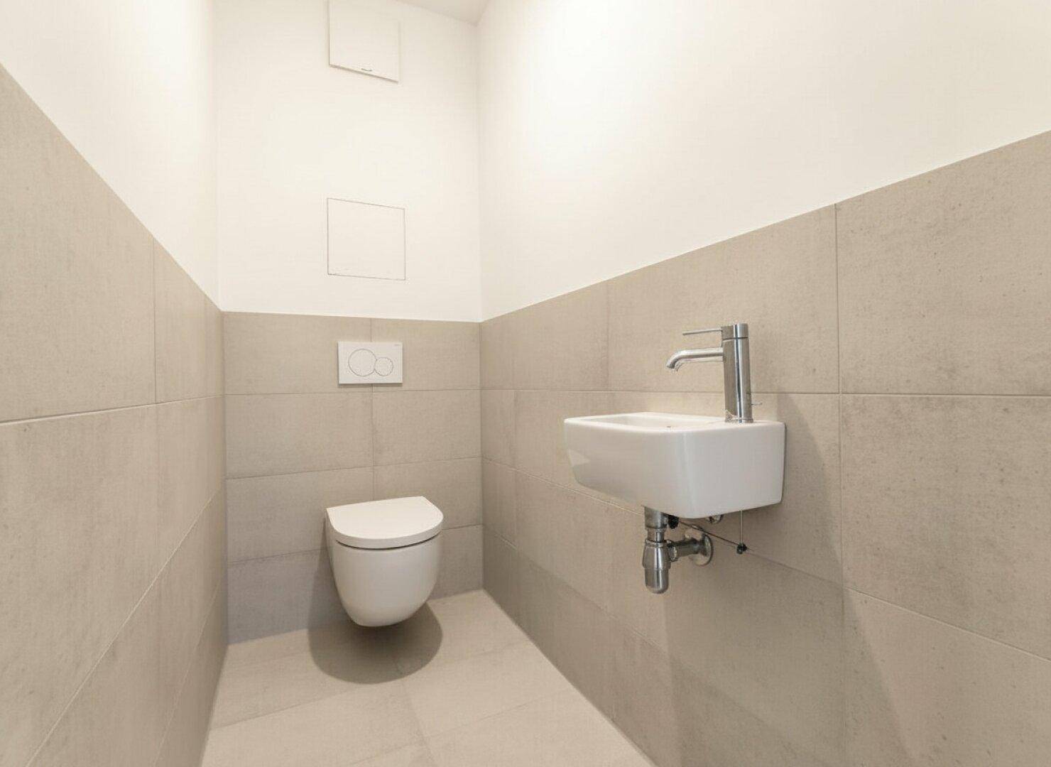 Modernes Gäste-WC mit Wand-WC und kleinem Waschbecken, ausgestattet mit hellen Fliesen.