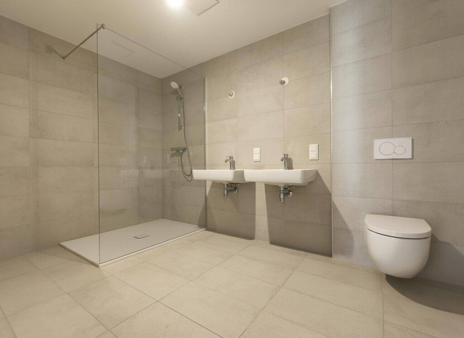 Modernes Badezimmer mit doppelten Waschbecken, ebenerdiger Dusche und hellen Fliesen.