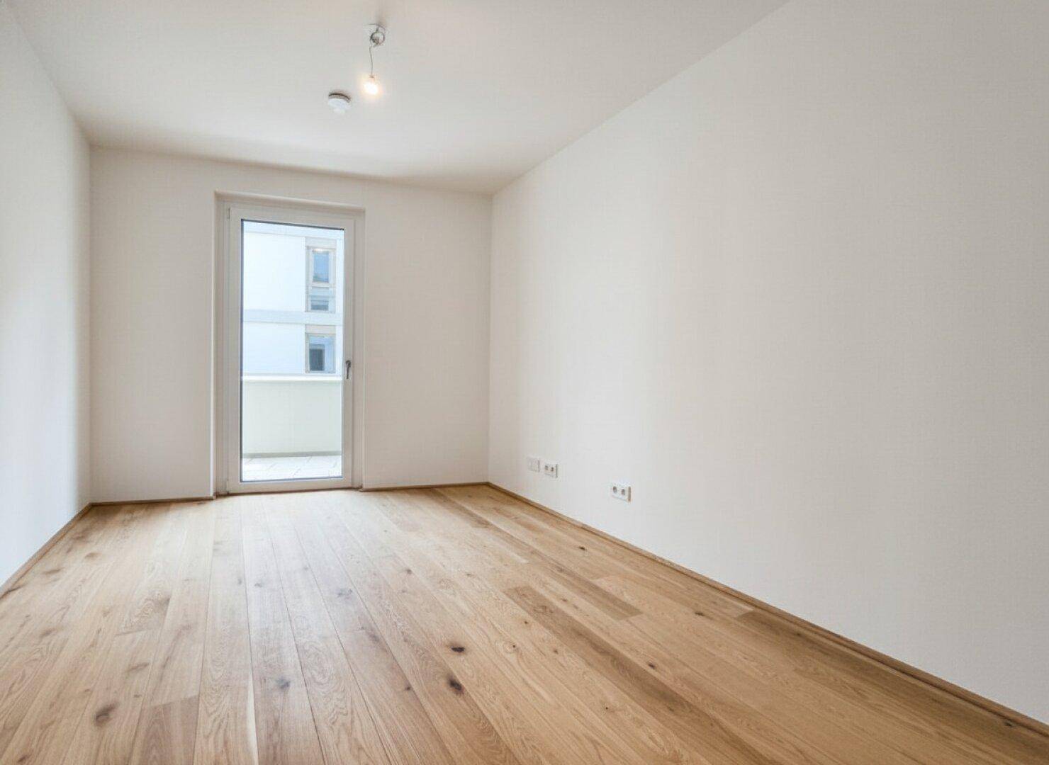 Geräumiges Schlafzimmer mit Holzboden und Balkonzugang, bereit für persönliche Einrichtung.