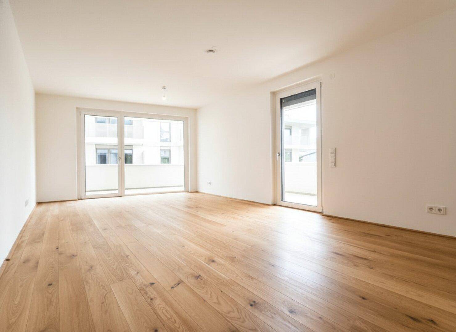 Geräumiges, helles Zimmer mit Parkettboden und zwei Balkonzugängen, bereit zur individuellen Gestaltung.