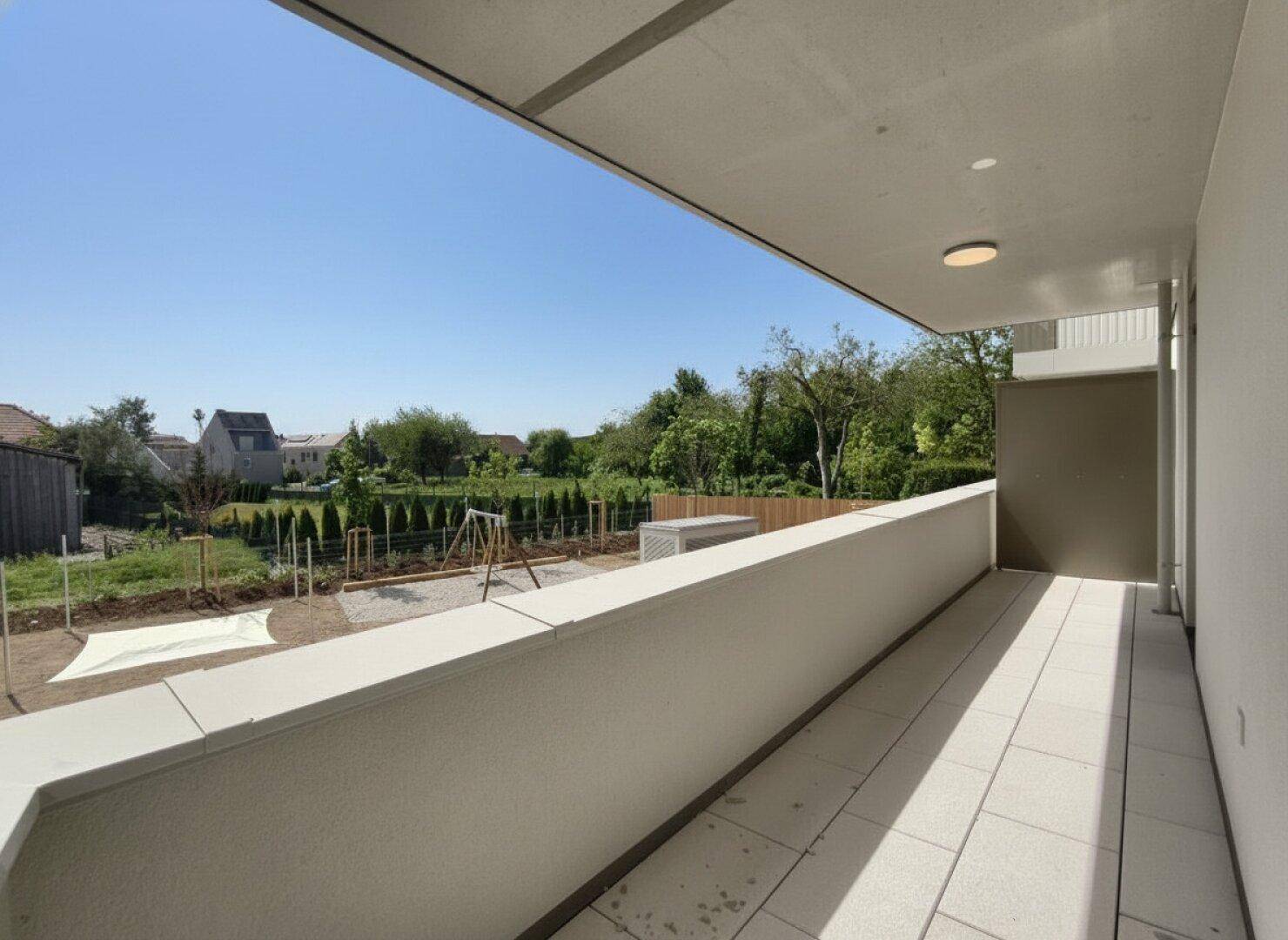 Langer Balkon mit Fliesenboden und Blick auf einen Gartenbereich mit Spielplatz.
