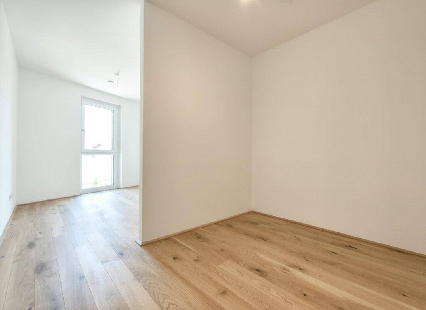 Helles, leeres Schlafzimmer mit Eichenparkett und einem großen Fenster.