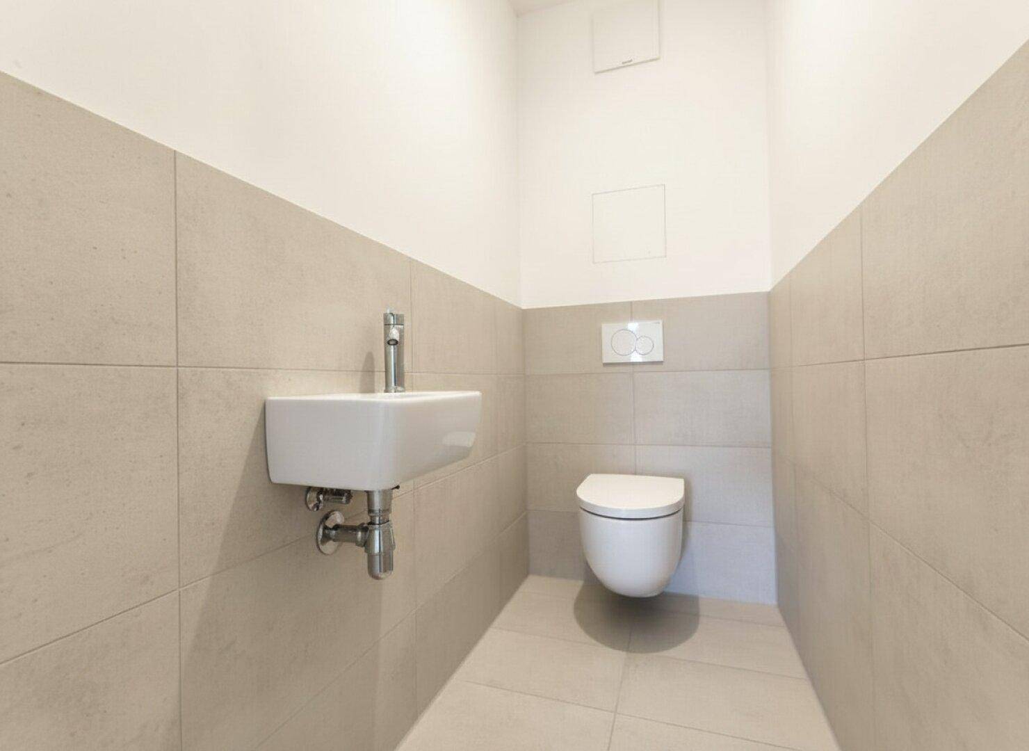Modernes Gäste-WC mit Wand-WC, kleinem Waschbecken und hellen Fliesen.