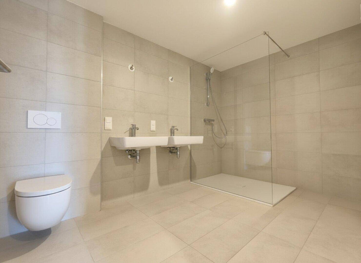 Modernes Badezimmer mit doppelten Waschbecken, großer begehbarer Dusche und hellen Fliesen.