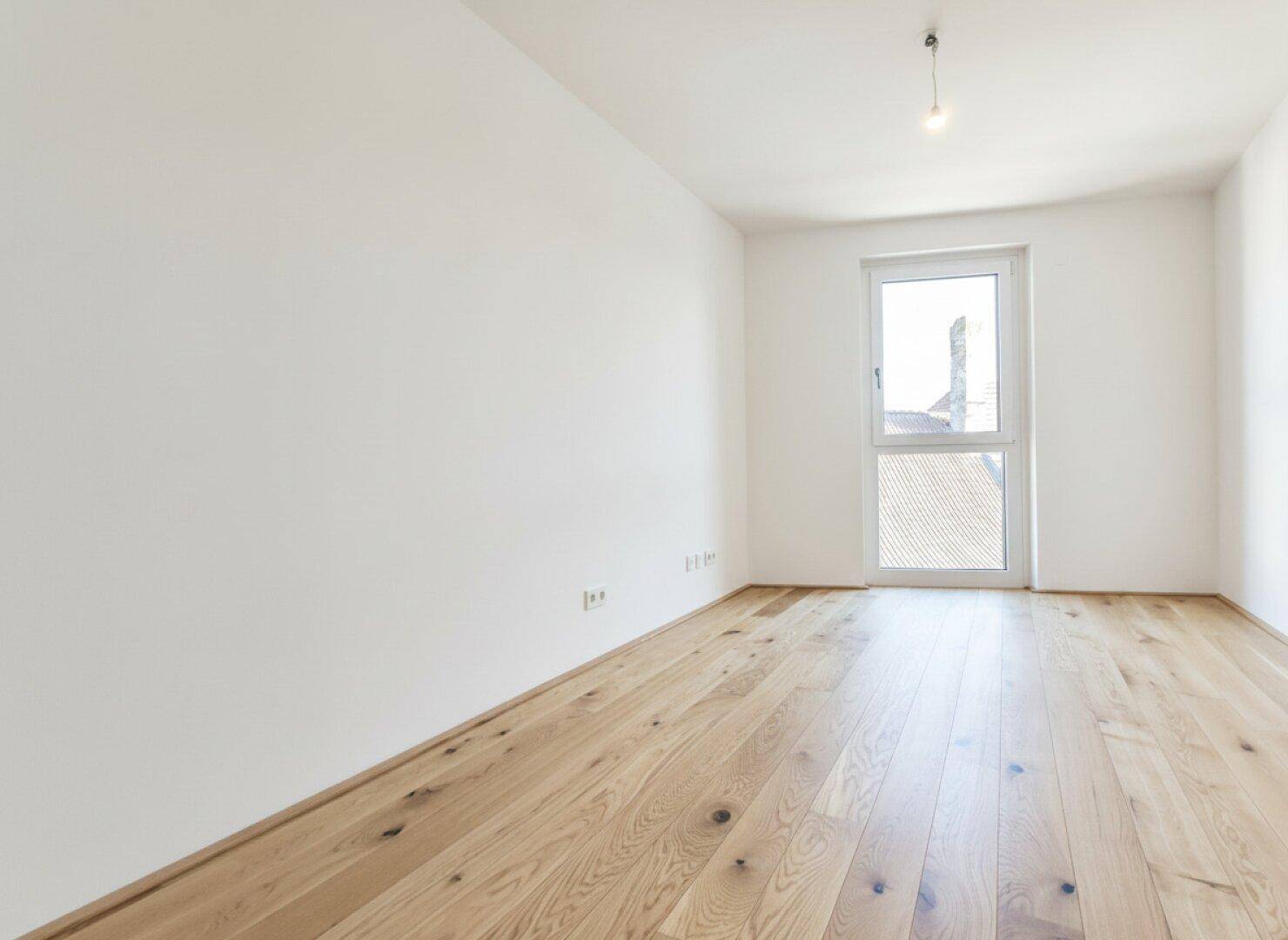 Geräumiges, unmöbliertes Schlafzimmer mit Eichenparkett und viel Tageslicht.