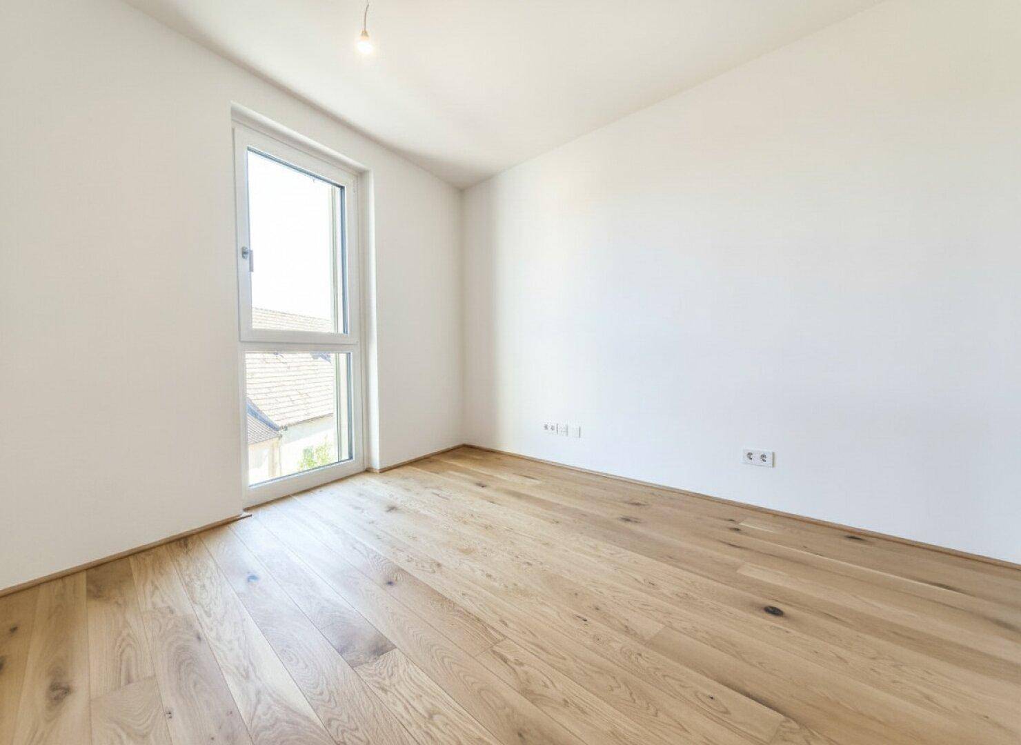 Helles Schlafzimmer mit Eichenparkettboden und einem hohen Fenster für viel Licht.