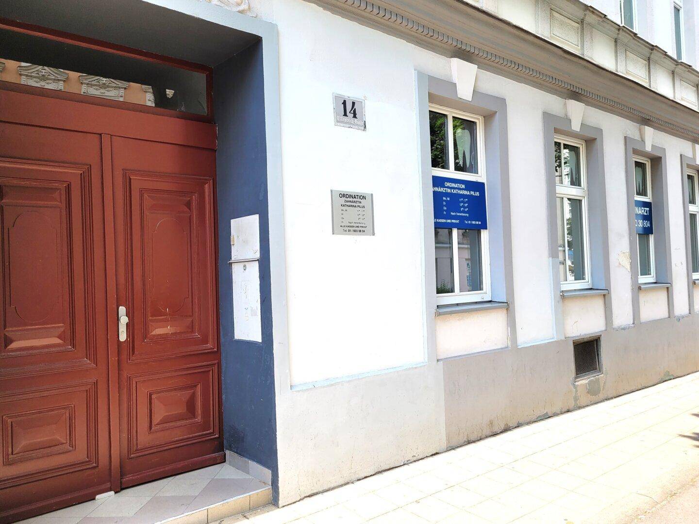 Detailansicht des Eingangs eines Altbaus mit großer Holztür und Hinweisschildern an der Fassade.