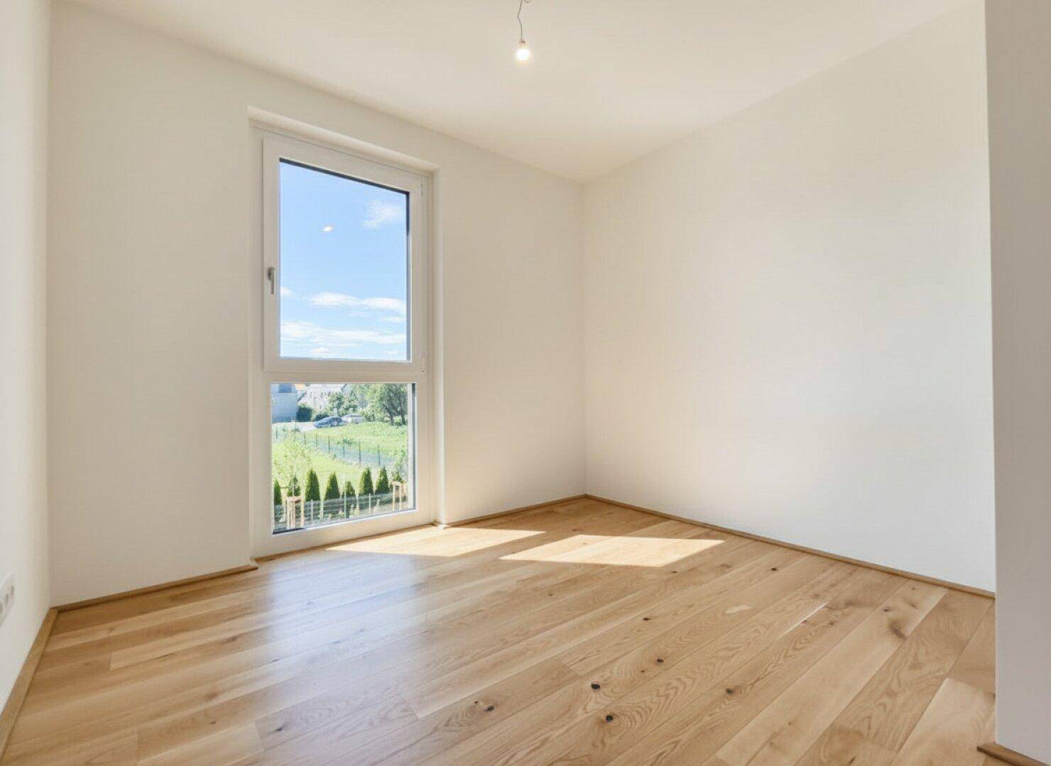 Ruhiges Schlafzimmer mit Holzboden und einem großen Fenster mit Blick ins Grüne.