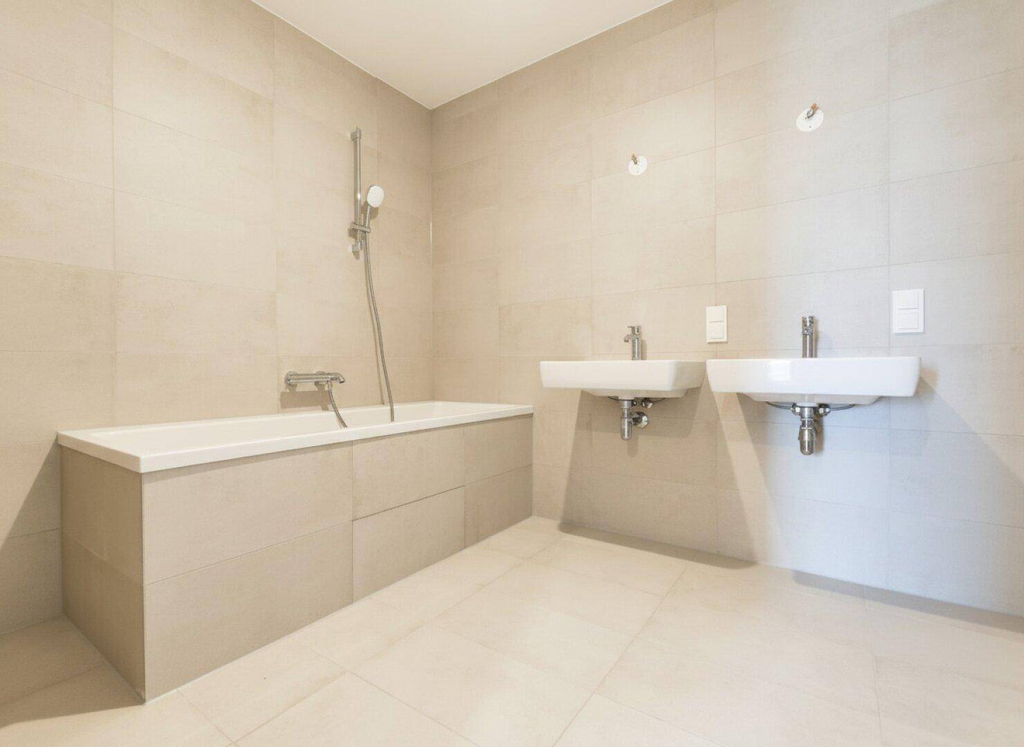 Modernes Badezimmer mit Badewanne, zwei Waschbecken und hellen Fliesen.