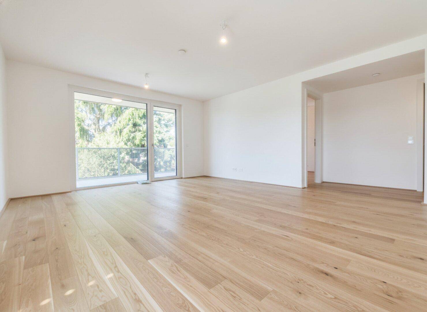 Helles, leeres Zimmer mit Eichenparkett und Zugang zu einem Balkon.