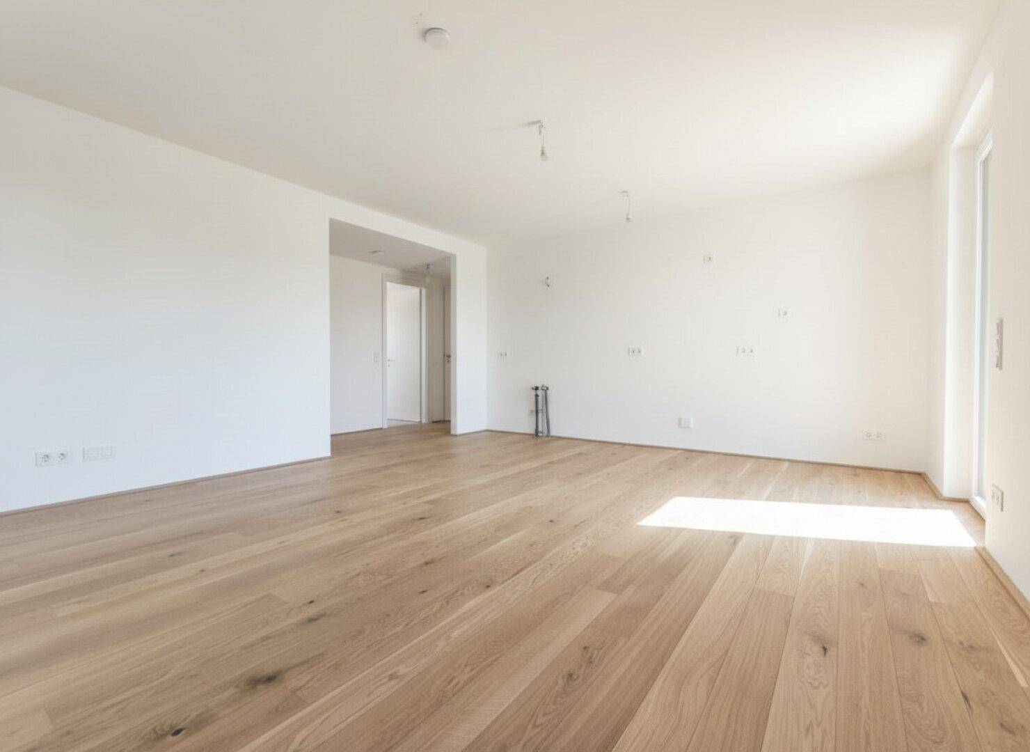 Geräumiges, unmöbliertes Zimmer mit hellem Parkettboden und weiß gestrichenen Wänden.