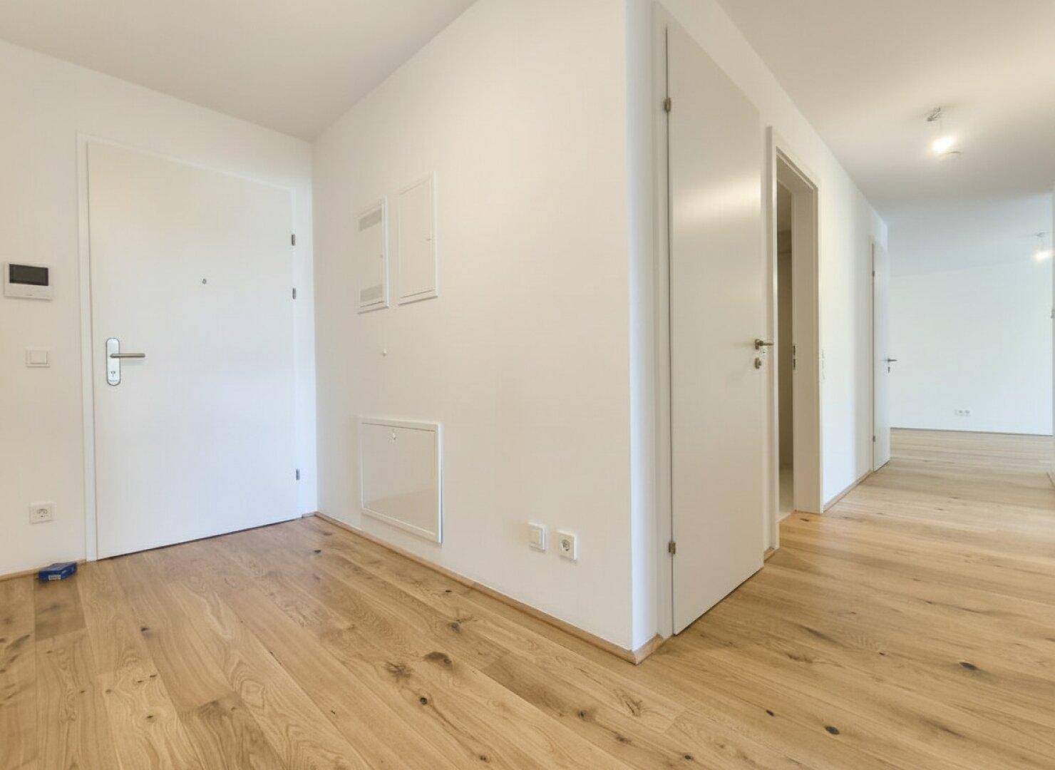 Heller Eingangsbereich mit Holzboden und weißen Türen, führt zu weiteren Räumen der Wohnung.