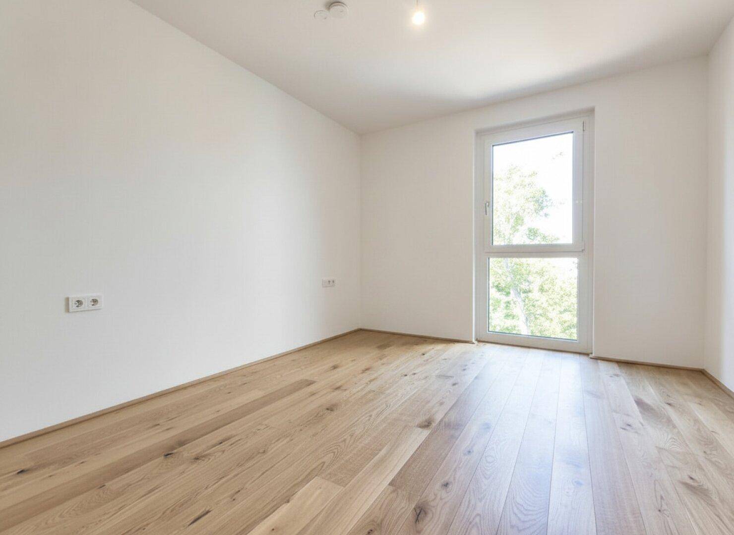 Unmöbliertes Zimmer mit Holzboden und Fenster, ideal für ein Kinder- oder Gästezimmer.