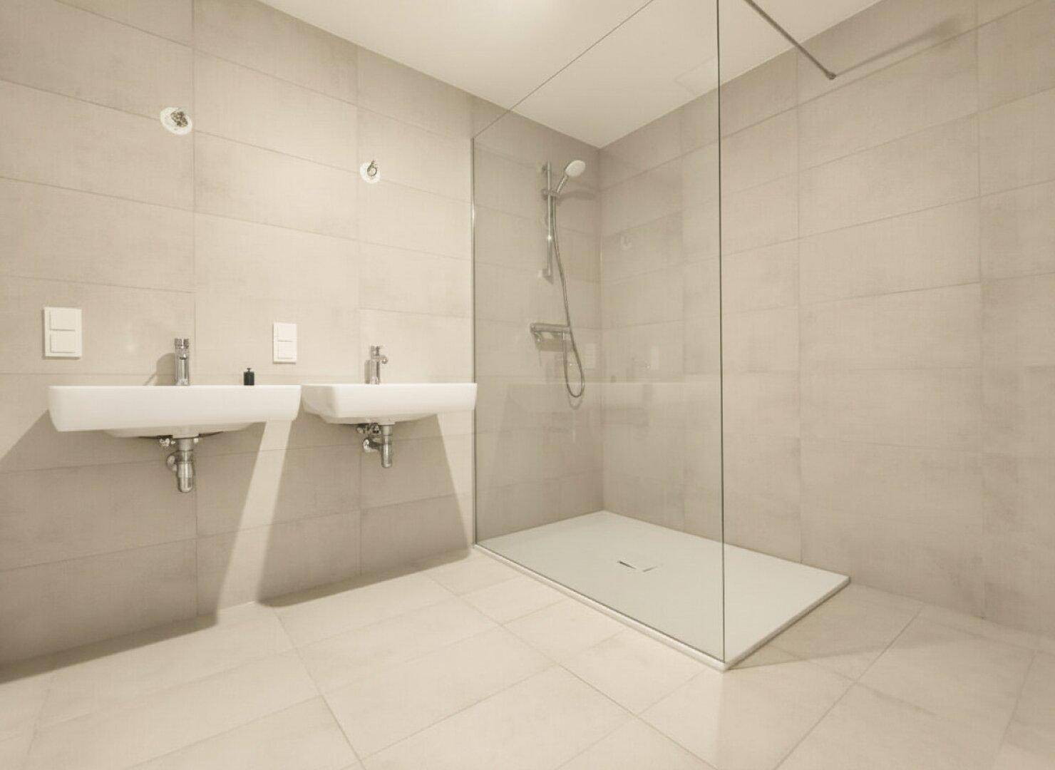 Modernes Badezimmer mit zwei Waschbecken und einer ebenerdigen Dusche, hell gefliest.