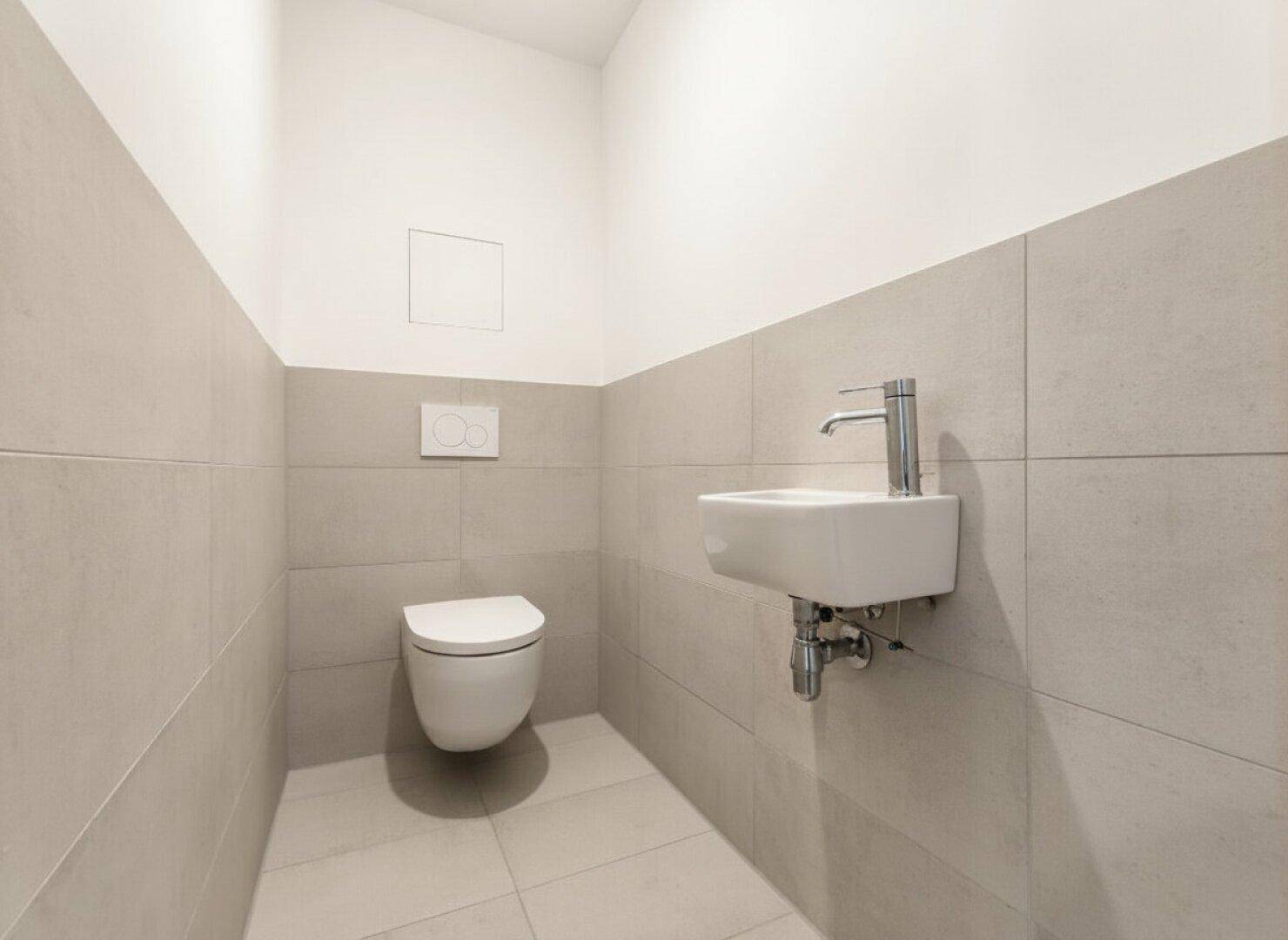 Gäste-WC mit wandhängender Toilette, kleinem Waschbecken und modernen Fliesen.