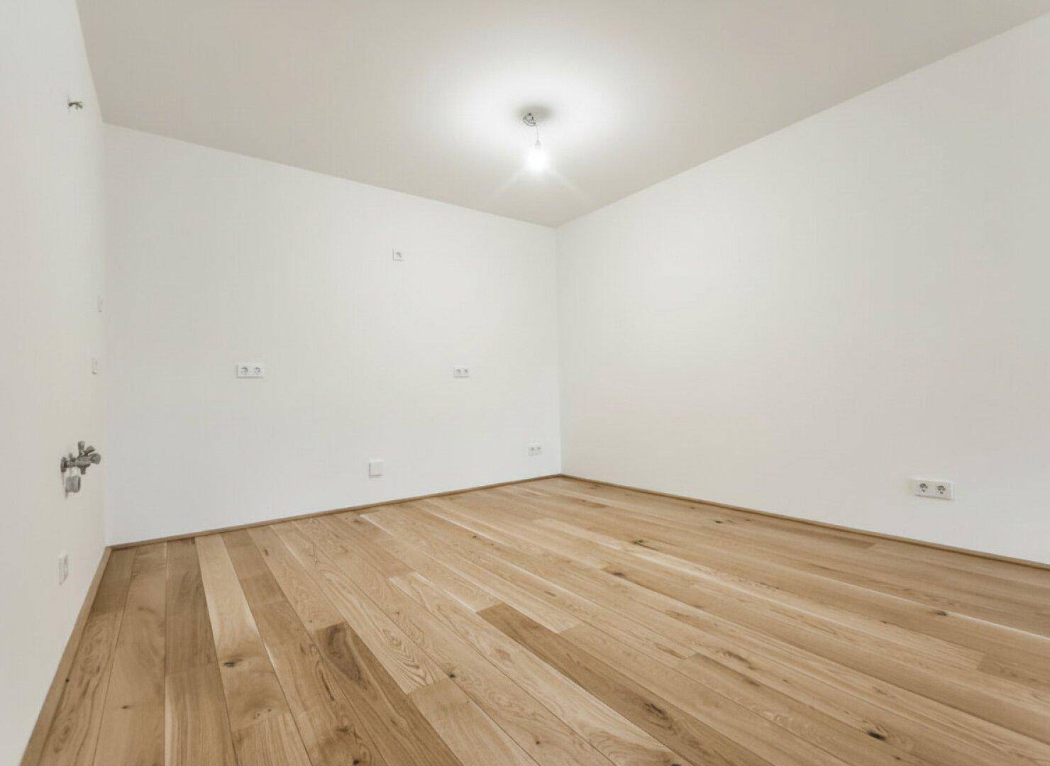 Leeres Zimmer mit Holzboden und weißen Wänden, ideal für Schlaf- oder Arbeitszimmer.