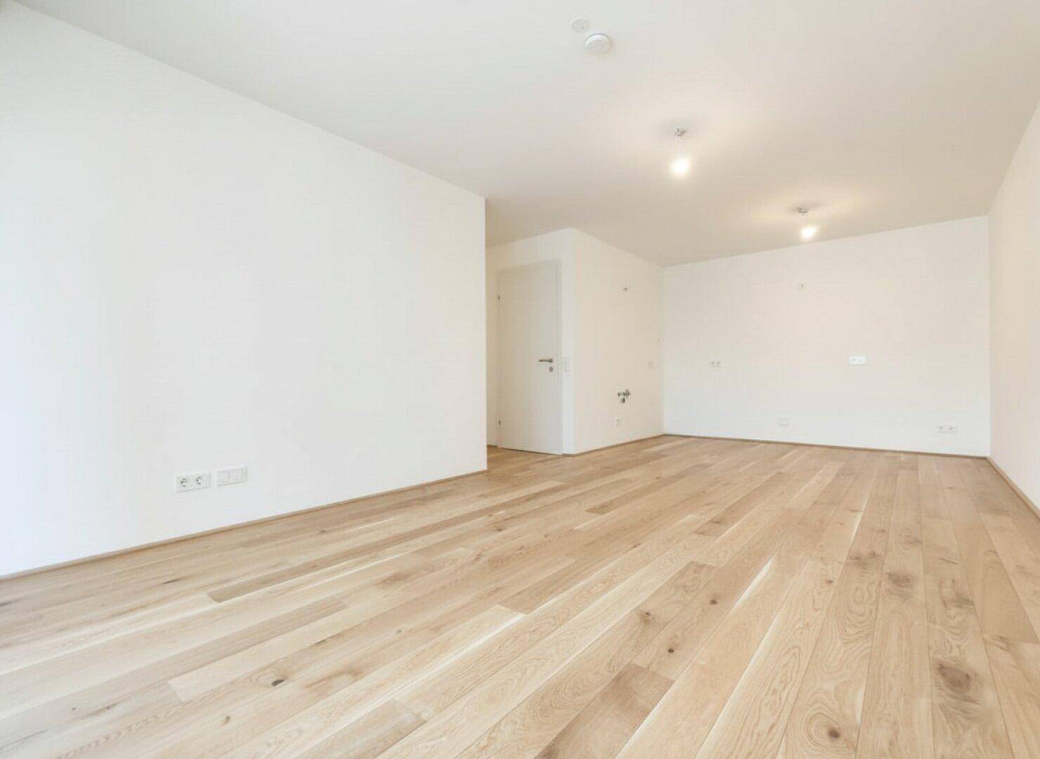 Heller Raum mit Holzboden und weißen Wänden, bereit zur individuellen Gestaltung und Einrichtung.