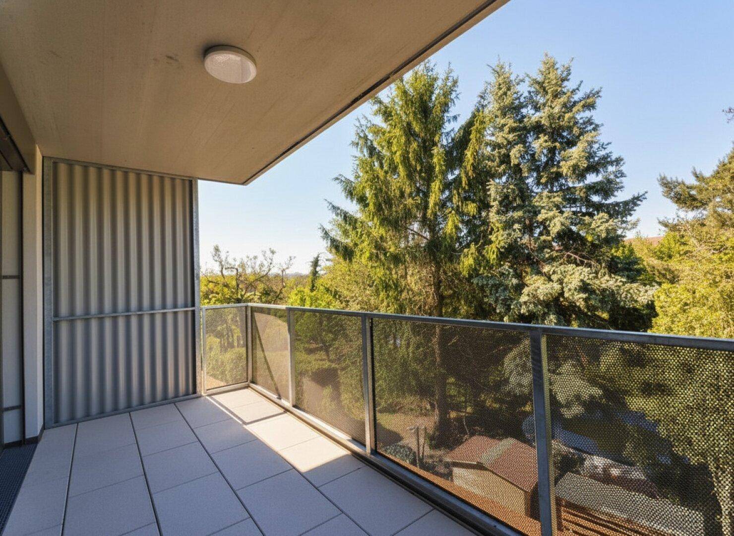 Geräumiger Balkon mit Fliesenboden und Metallgeländer, bietet einen schönen Blick ins Grüne.