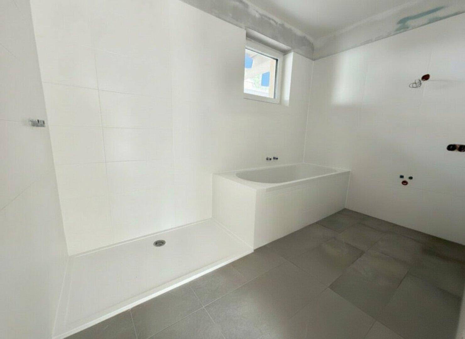 Unfertiges Badezimmer mit Badewanne und ebenerdiger Dusche in einem Neubau.