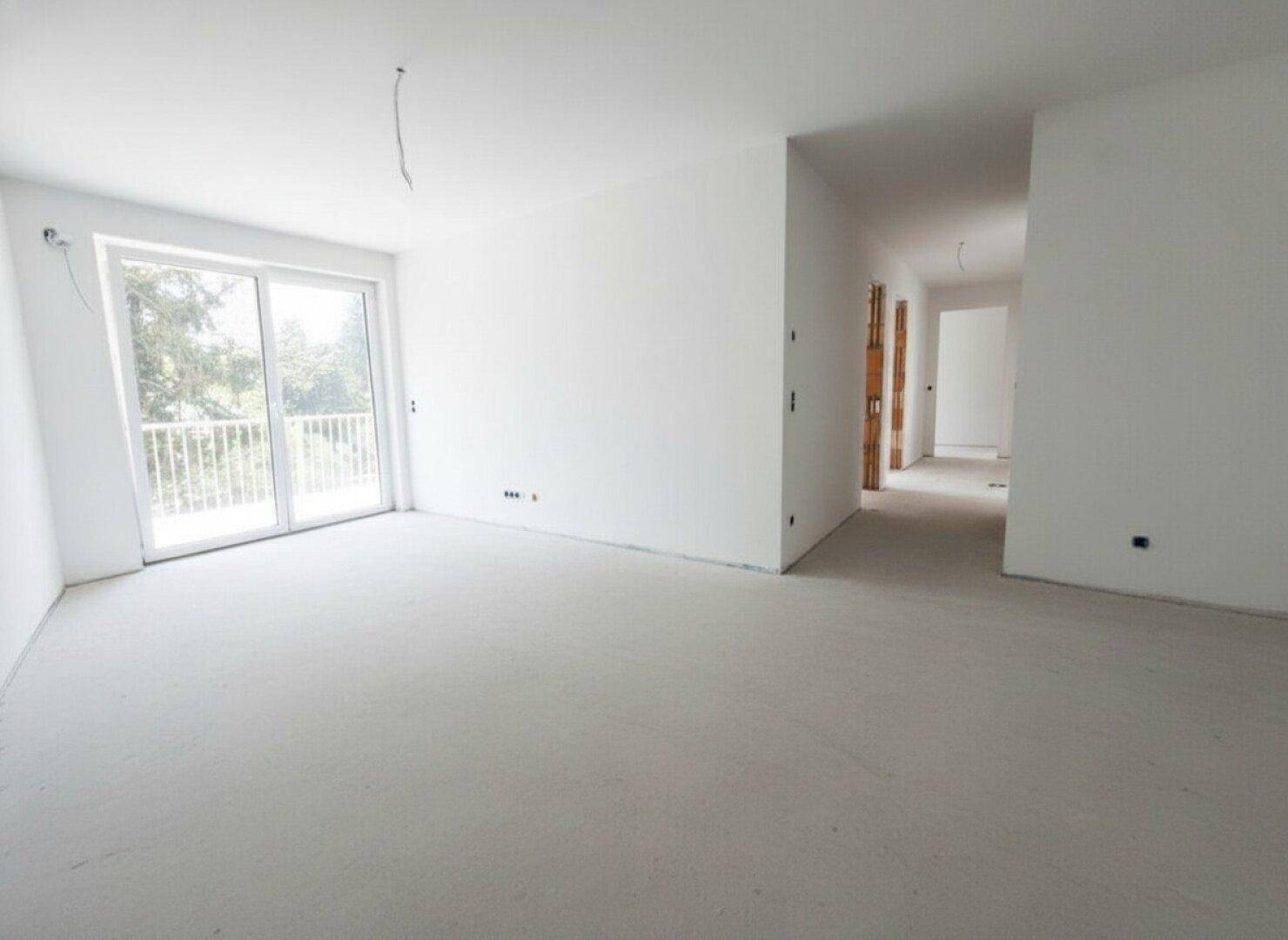 Unfertiger Wohnraum mit weißen Wänden und großem Schiebetürzugang zu einem Balkon, bereit für den Ausbau.
