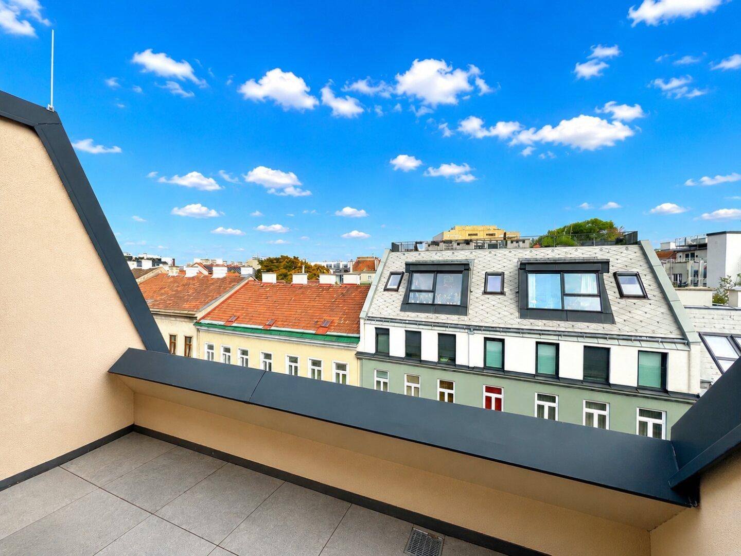 Dachterrasse mit Fliesenboden und weitem Blick über die Dächer der Stadt unter blauem Himmel.