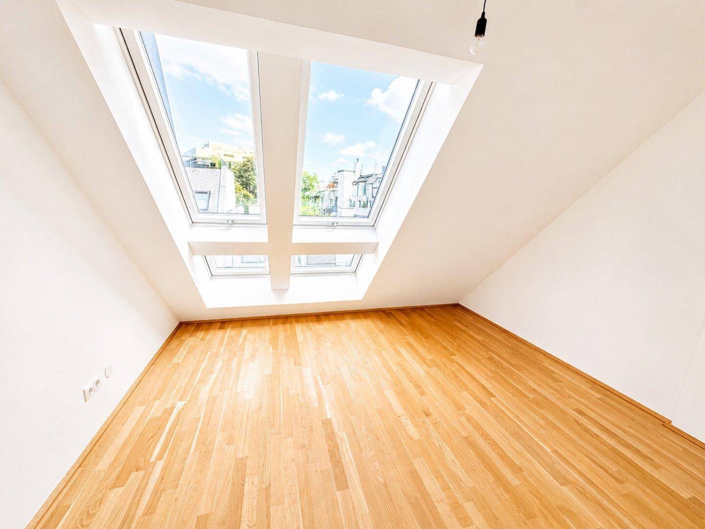 Lichtdurchfluteter Raum im Dachgeschoss mit Holzboden und zwei großen Dachfenstern für optimale Belichtung.