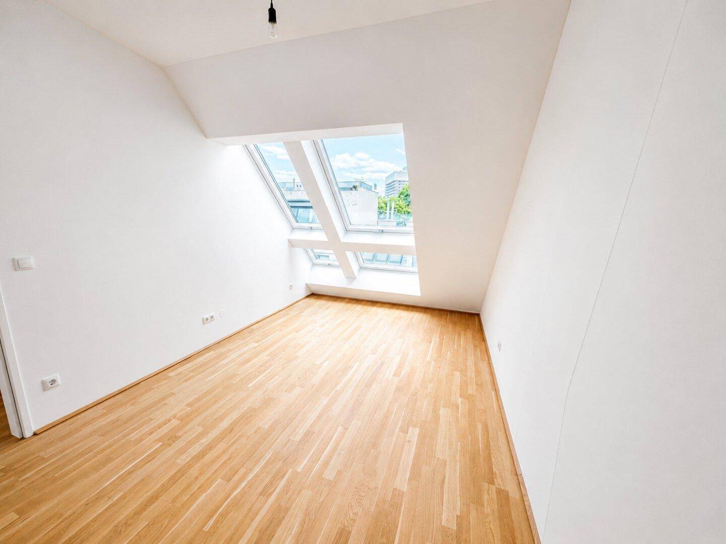 Gemütlicher Dachgeschossraum mit Holzboden und einem großen Dachfenster, das den Raum erhellt.