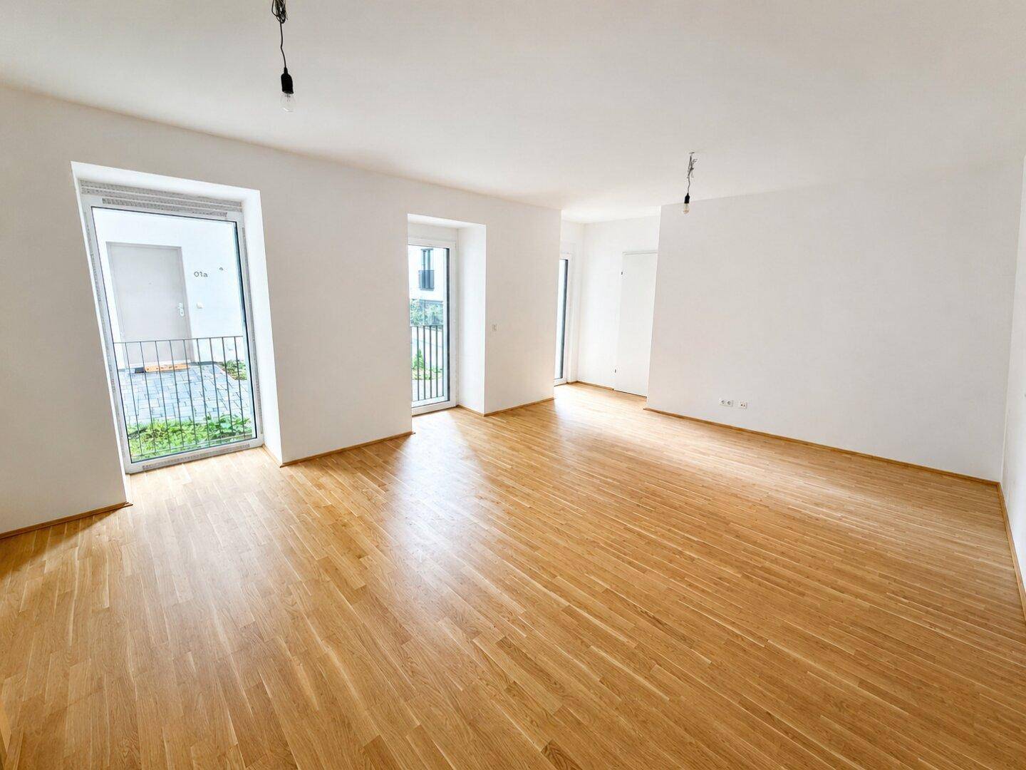 Geräumiges, unmöbliertes Zimmer mit hellem Parkettboden und großen Fenstern.