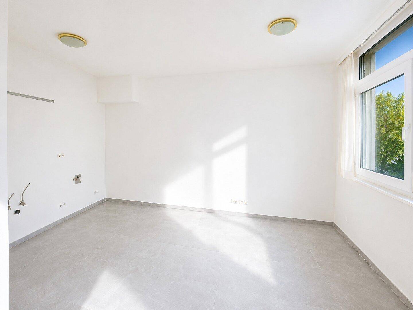 Heller, leerer Raum mit großen Fenstern und Anschlüssen an der Wand, bereit für die Einrichtung.