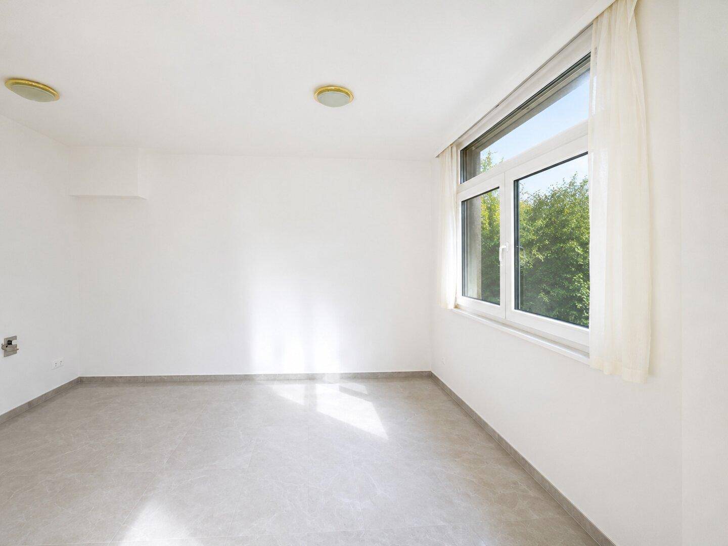 Geräumiger, heller Innenraum mit Fliesenboden und einem großen Fenster, das viel Tageslicht hereinlässt.