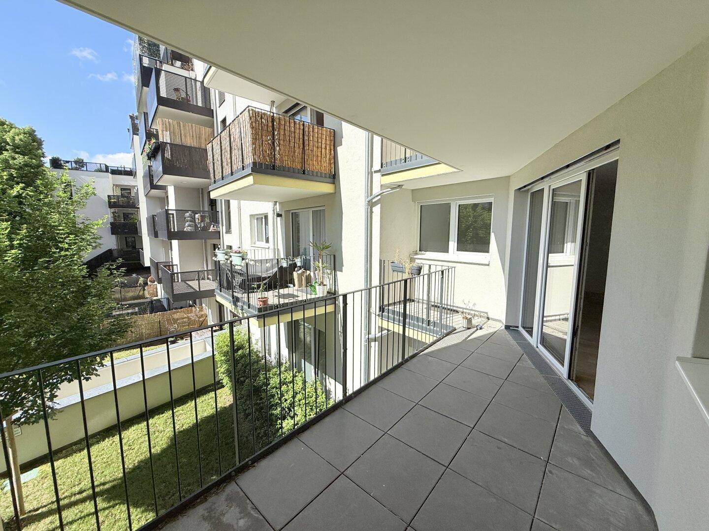 Moderner Balkon mit Fliesenboden und Blick auf den Innenhof und weitere Balkone.