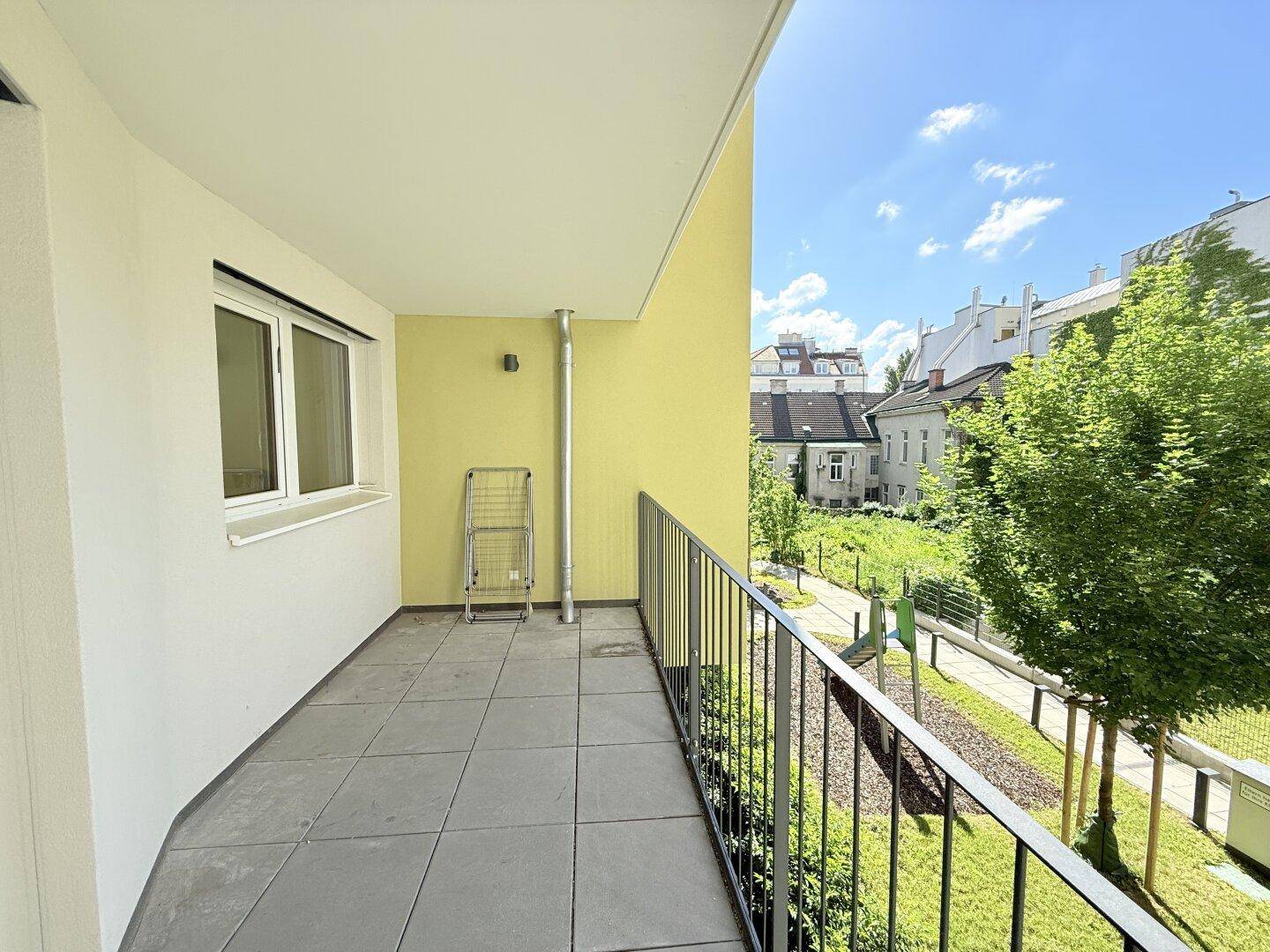 Langer Balkon mit Fliesenboden und Blick auf den begrünten Innenhof.