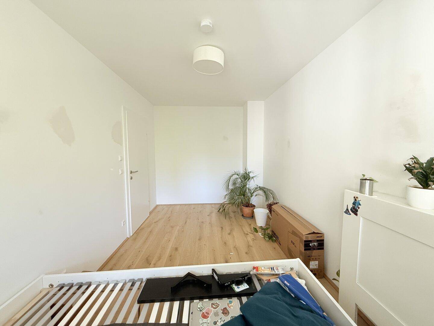 Helles Schlafzimmer mit Holzboden und einem Bettgestell, das auf die Fertigstellung wartet.