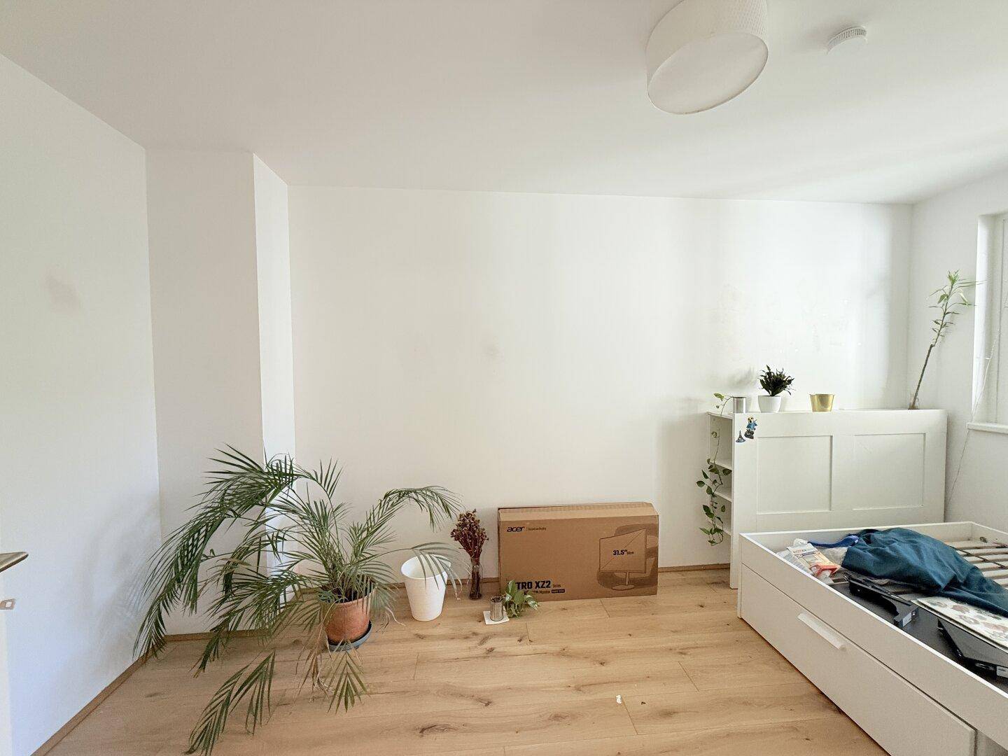 Geräumiges Schlafzimmer mit Parkettboden, Pflanzen und einem Bettgestell, das auf die Einrichtung wartet.